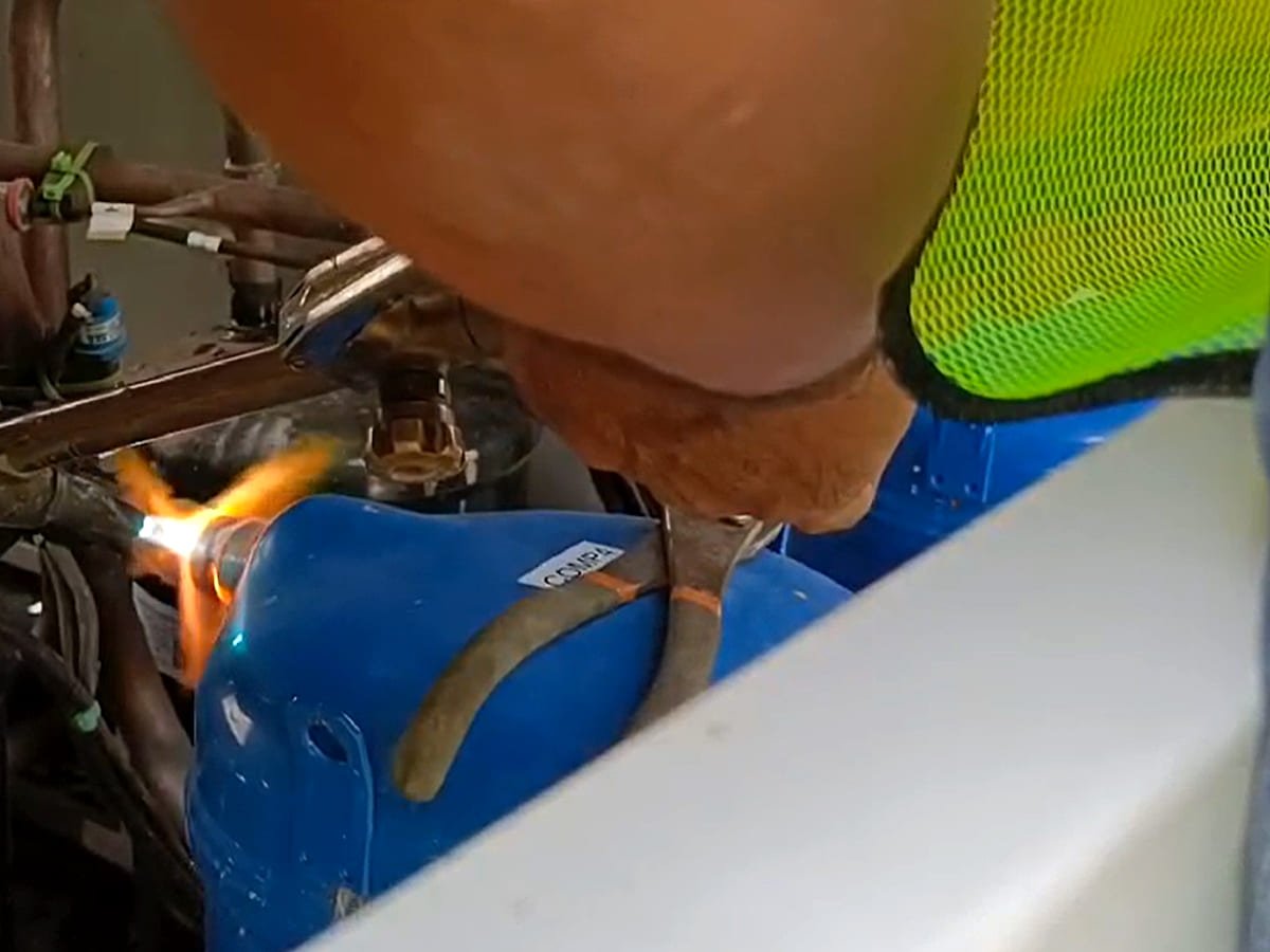 Brazing torch flame on a copper joint during a compressor replacement